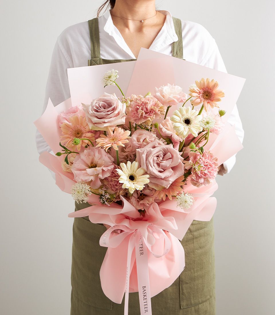 Romantic blush mixed bouquet of roses, gerberas, and carnations in soft pink and cream tones, wrapped in pink paper with