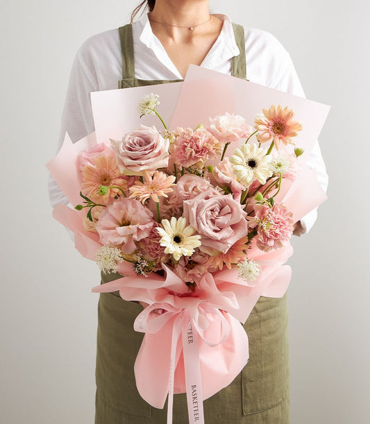 Romantic blush mixed bouquet of roses, gerberas, and carnations in soft pink and cream tones, wrapped in pink paper with