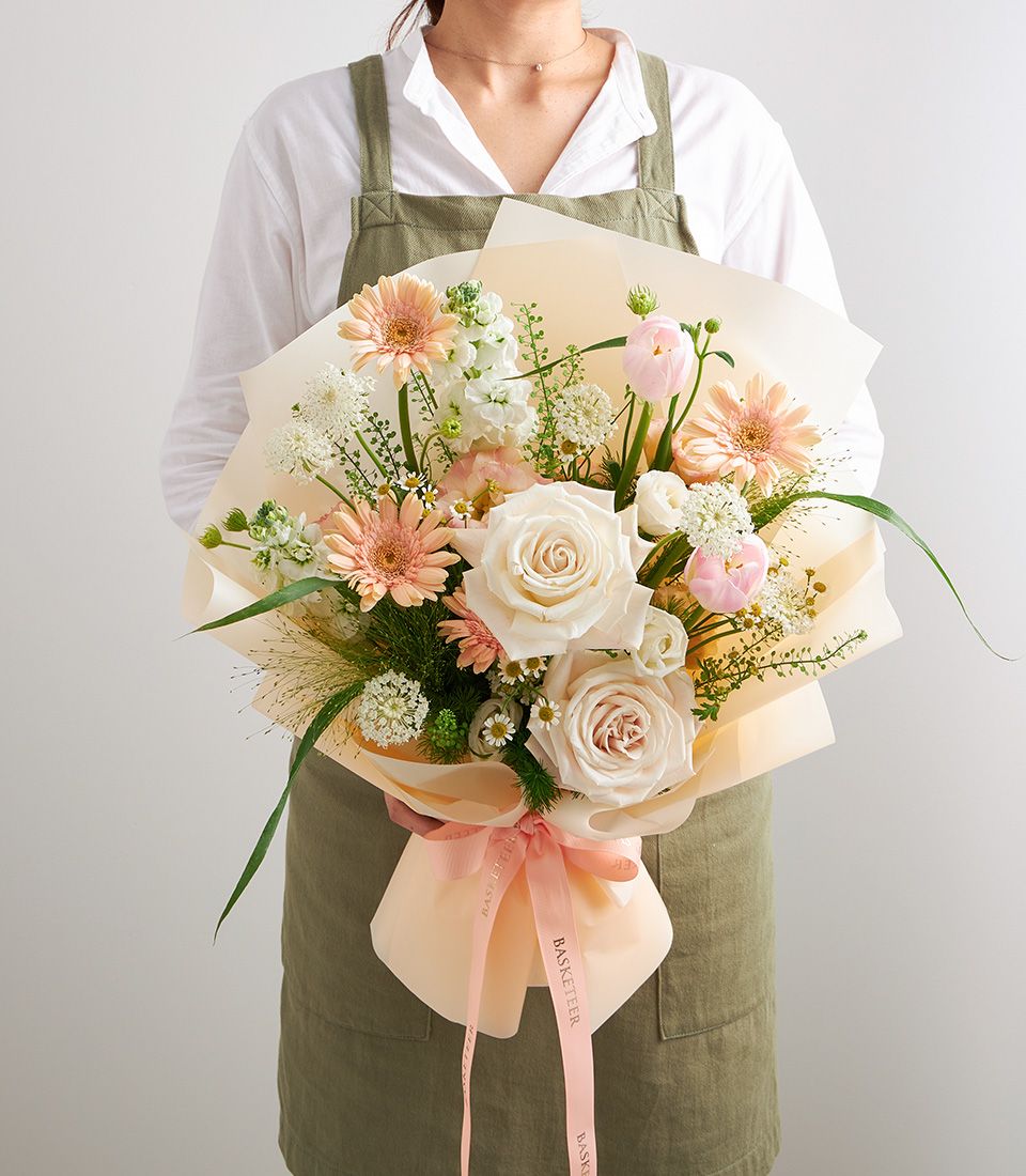 Florist holding mixed pastel bouquet with pink gerberas, roses, and tulips in peach paper wrapping