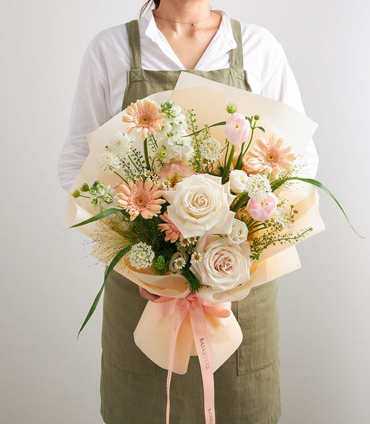 Florist holding mixed pastel bouquet with pink gerberas, roses, and tulips in peach paper wrapping