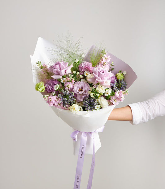 Hand-held purple pastel mixed bouquet with roses, lavender, and green foliage in white wrap