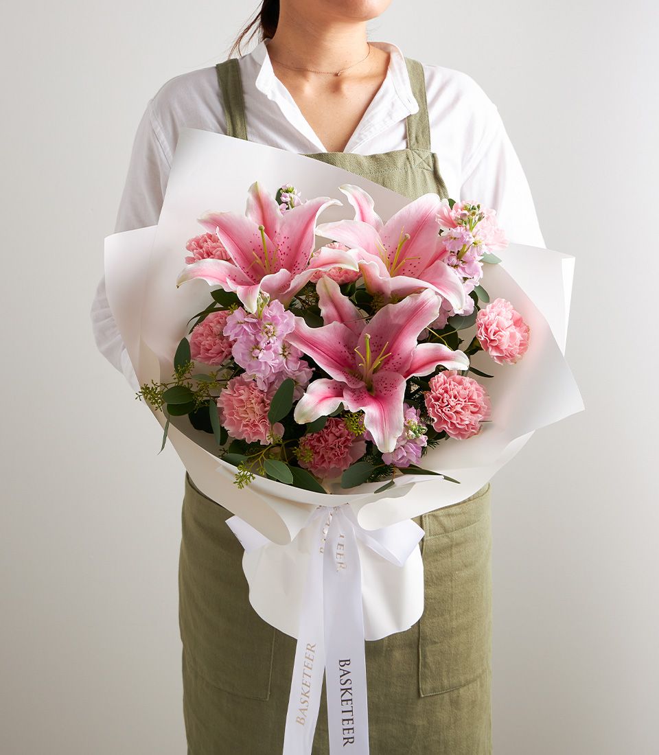Pink stargazer lily bouquet with carnations and stock flowers, wrapped in white paper with gold ribbon
