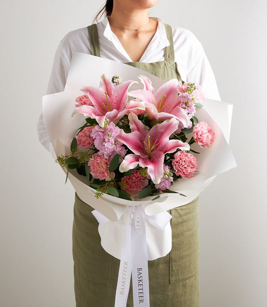 Pink stargazer lily bouquet with carnations and stock flowers, wrapped in white paper with gold ribbon