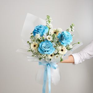 Vibrant blue roses with white daisies and greenery, wrapped in cellophane with light blue ribbon