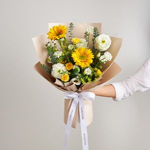 Vibrant yellow gerbera daisies and white ranunculus sunflower bouquet wrapped in kraft paper with white ribbon