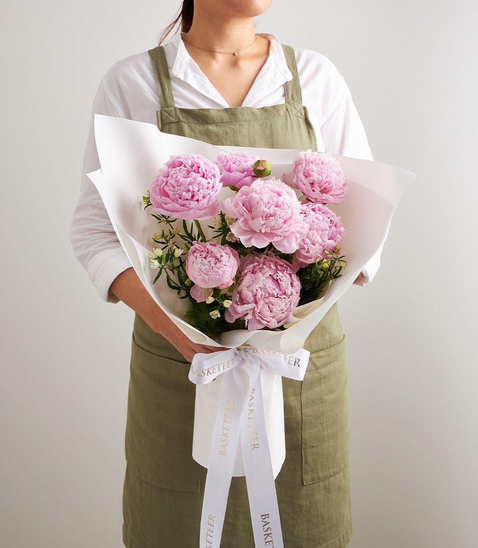 Florist holding pink peony bouquet with white wrapping and gold-ribbon detail