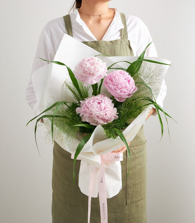 Petite pink peony bouquet with green foliage and white wrapping tied with Basketeer ribbon