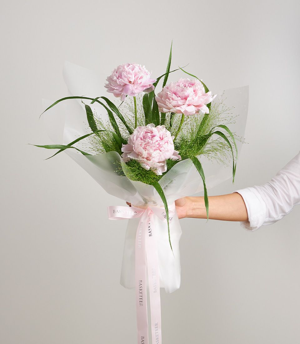 Light pink peony bouquet with green foliage in white paper wrap and ribbon bow