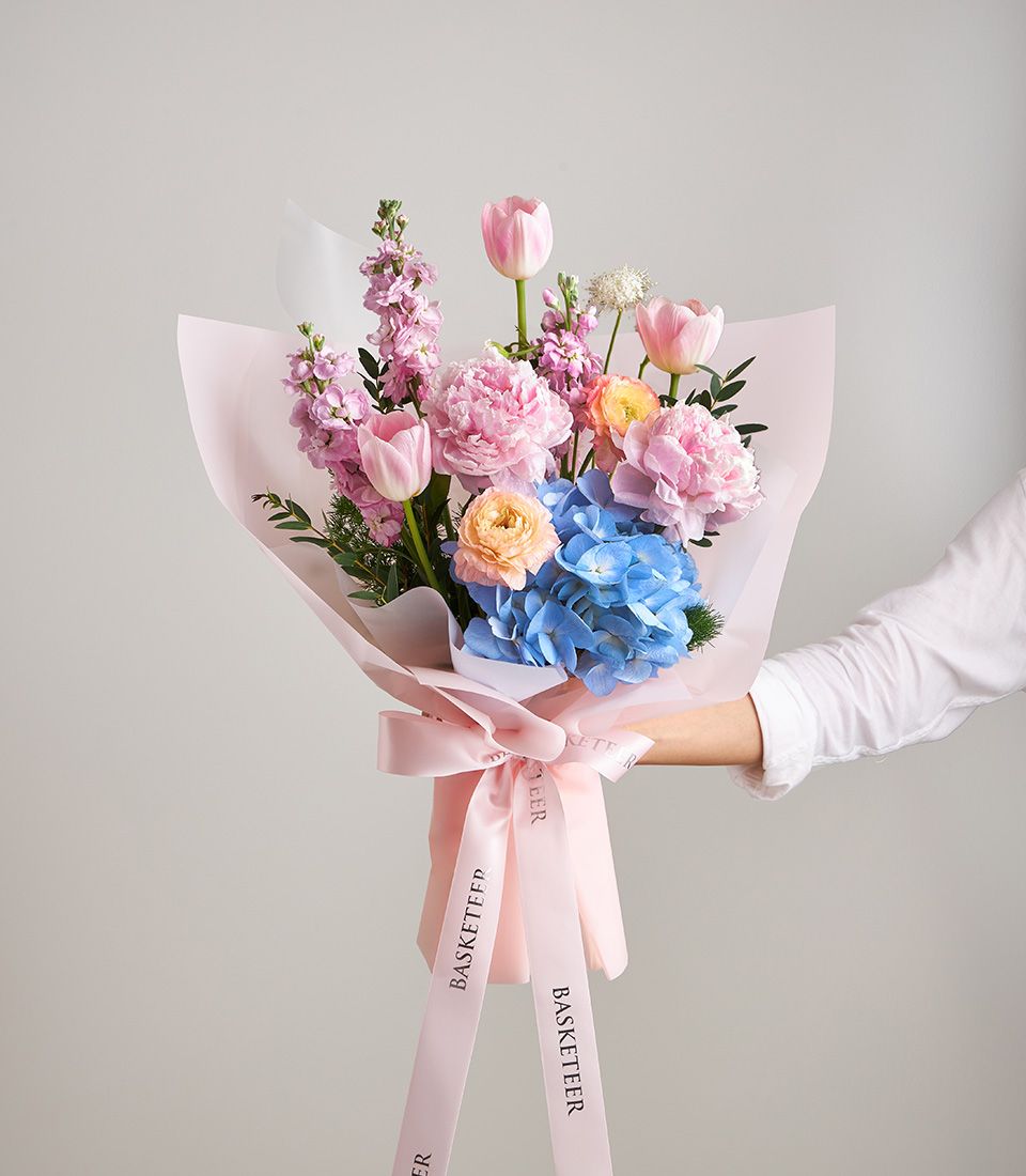 Blush pink peony and tulip bouquet with blue hydrangea, wrapped in soft pink paper with ribbon bow