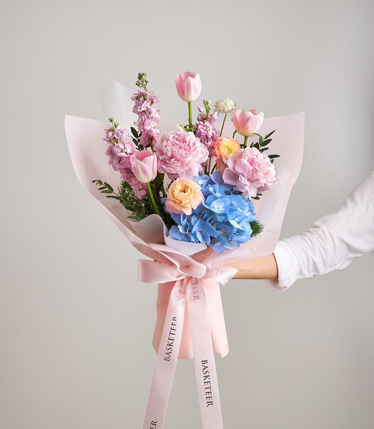 Blush pink peony and tulip bouquet with blue hydrangea, wrapped in soft pink paper with ribbon bow