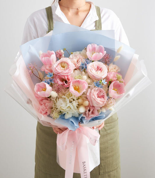 Pastel pink tulips, garden roses, and white hydrangeas in luxury birthday flower bouquet with ribbon wrap