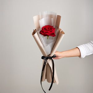 Single red rose with white and kraft paper wrapping, black satin ribbon accent