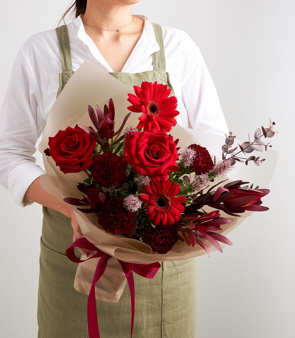 Vibrant red rose and gerbera bouquet wrapped in kraft paper with deep red ribbon