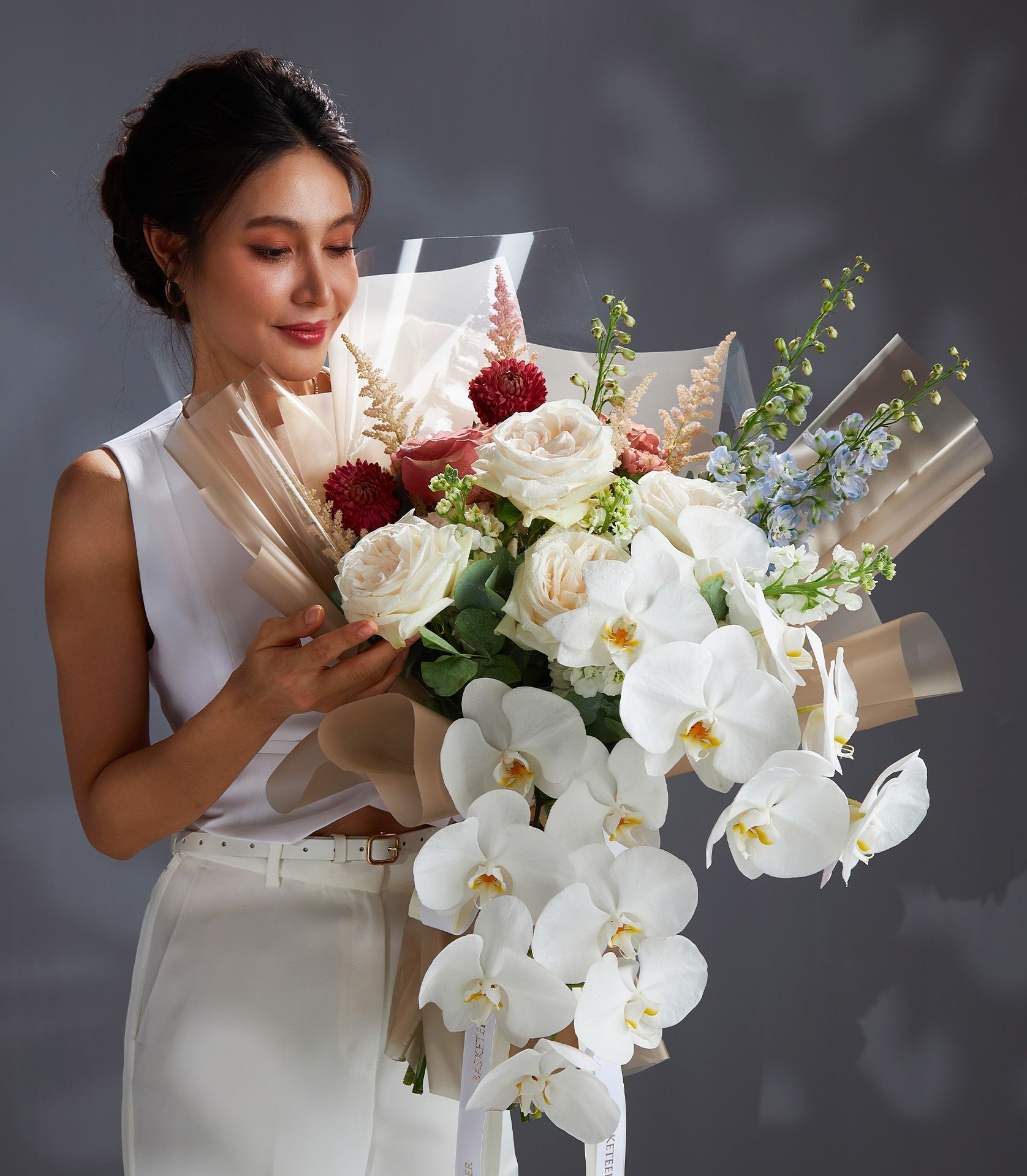 Luxury rose and orchid bouquet with dahlias, delphiniums, and astilbe in white, pink, and red tones, wrapped in kraft paper