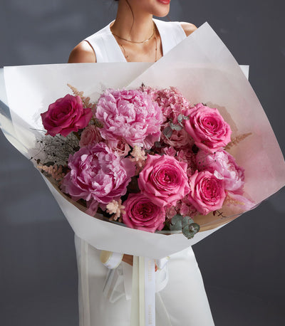 Luxury pink peony and rose bouquet with eucalyptus, wrapped in white paper and cream ribbon