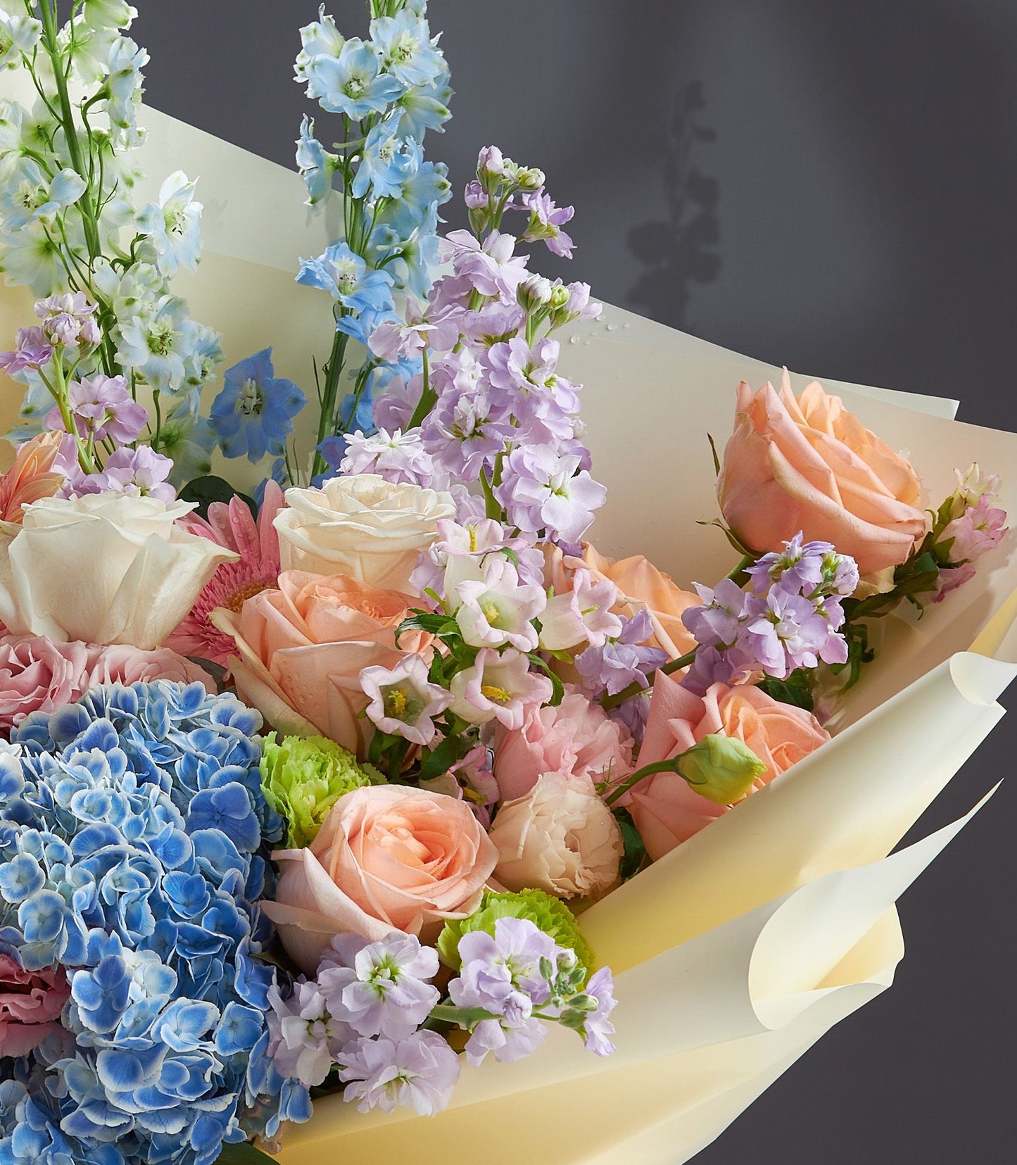 Pastel rose and hydrangea bouquet with delphiniums and gerbera daisies in cream wrapping