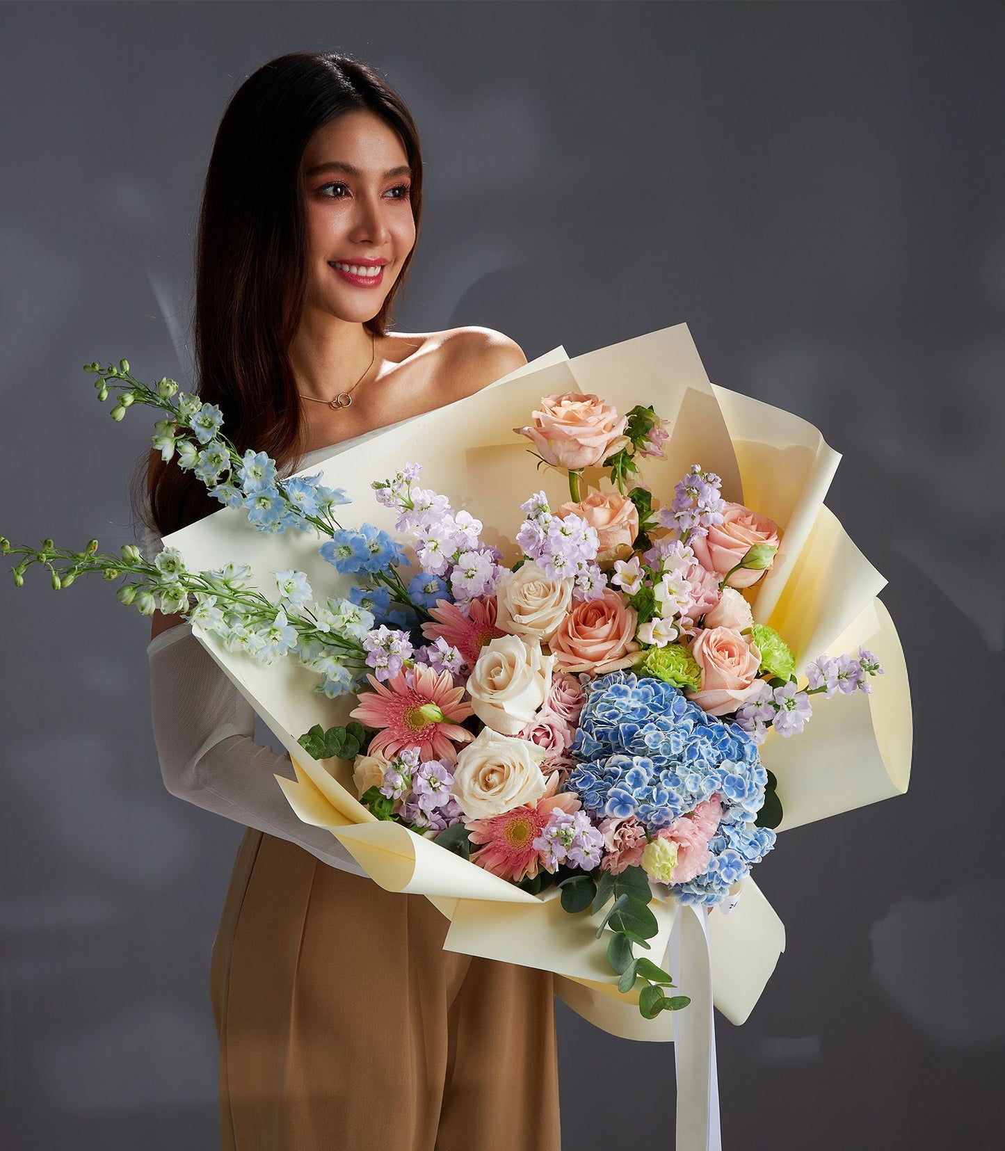 Woman holding pastel rose and hydrangea bouquet wrapped in yellow paper with white ribbon