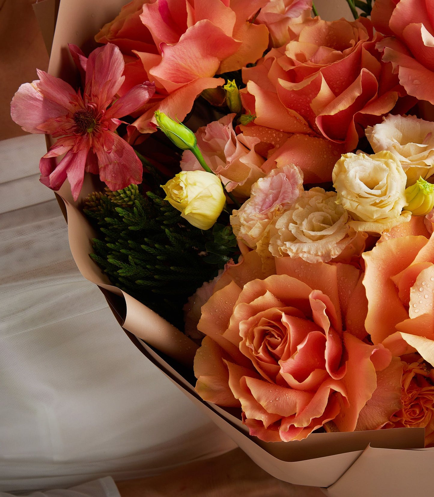 Sunset orange and coral roses with cream ranunculus and dark pink accents in fresh flower bouquet