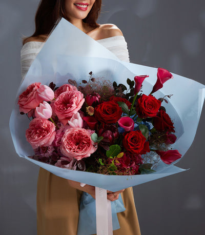 Vibrant red and pink rose luxury bouquet with garden roses, tulips, and calla lilies in light blue wrapping