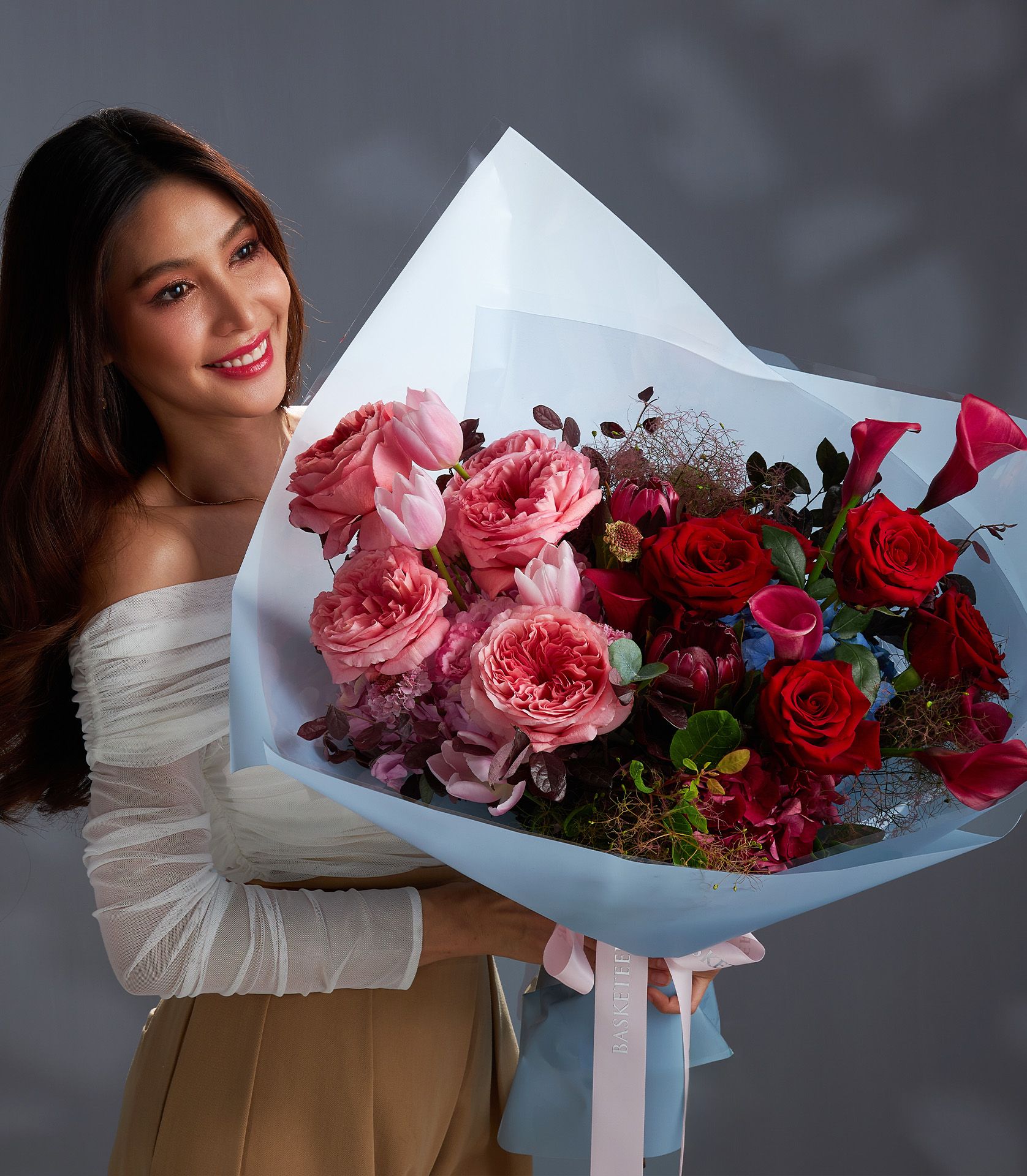 Woman holding luxury red and pink rose bouquet with garden roses, tulips, and calla lilies wrapped in blue paper