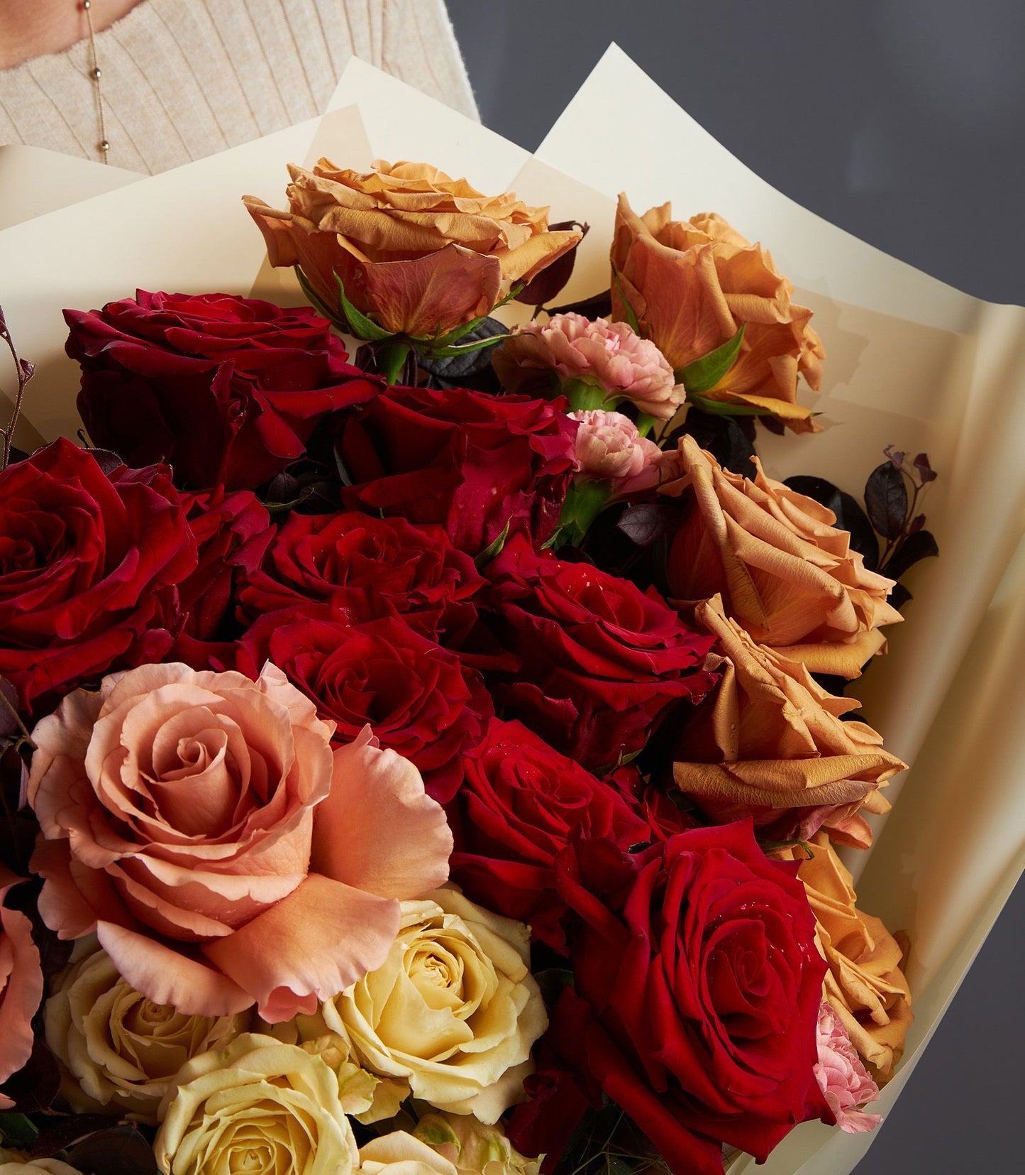Fresh Ecuador rose bouquet in deep red, peach, and yellow with carnation accents, wrapped in cream paper