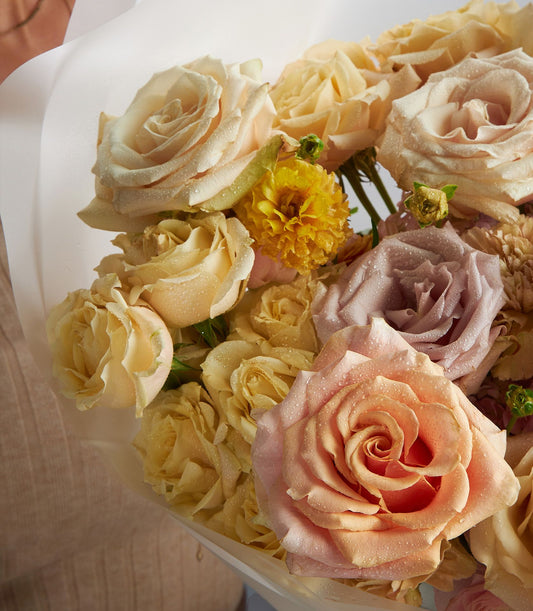 Fresh blush rose bouquet with pale yellow ranunculus, wrapped in cellophane for gifting