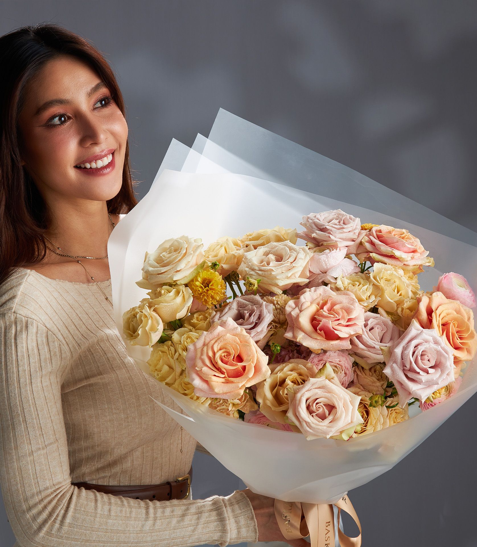 Woman holding premium blush rose bouquet with peach, pink, cream roses and accent flowers in white wrapped presentation