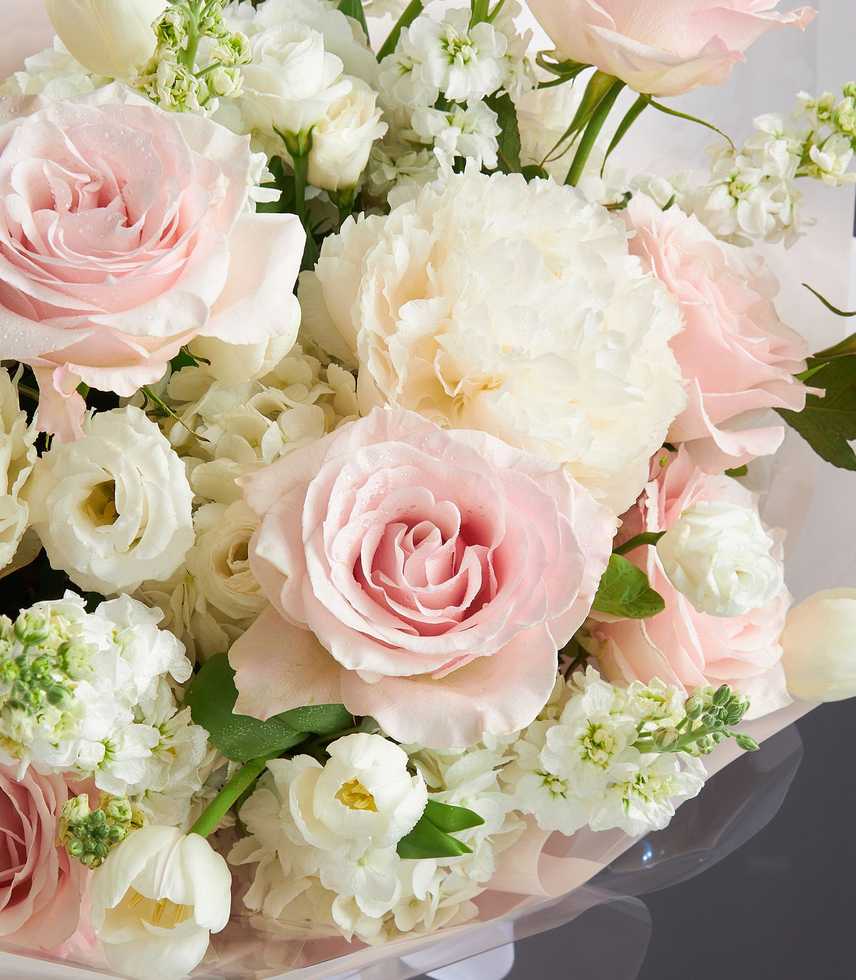 Light pink roses and white peonies bouquet with hydrangea and greenery, wrapped in peach paper