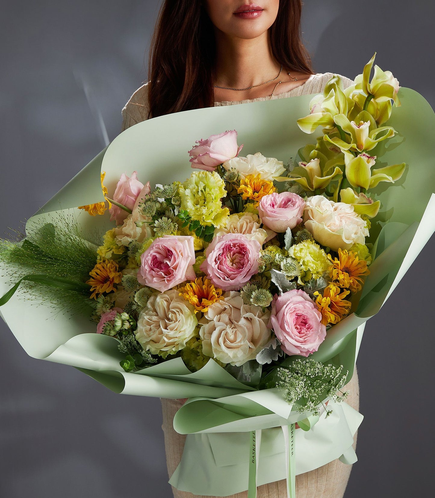 Pastel mixed flower bouquet with soft pink roses, yellow chrysanthemums, and green orchids in mint wrapping