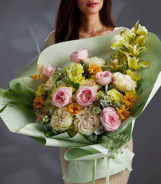 Pastel mixed flower bouquet with soft pink roses, yellow chrysanthemums, and green orchids in mint wrapping