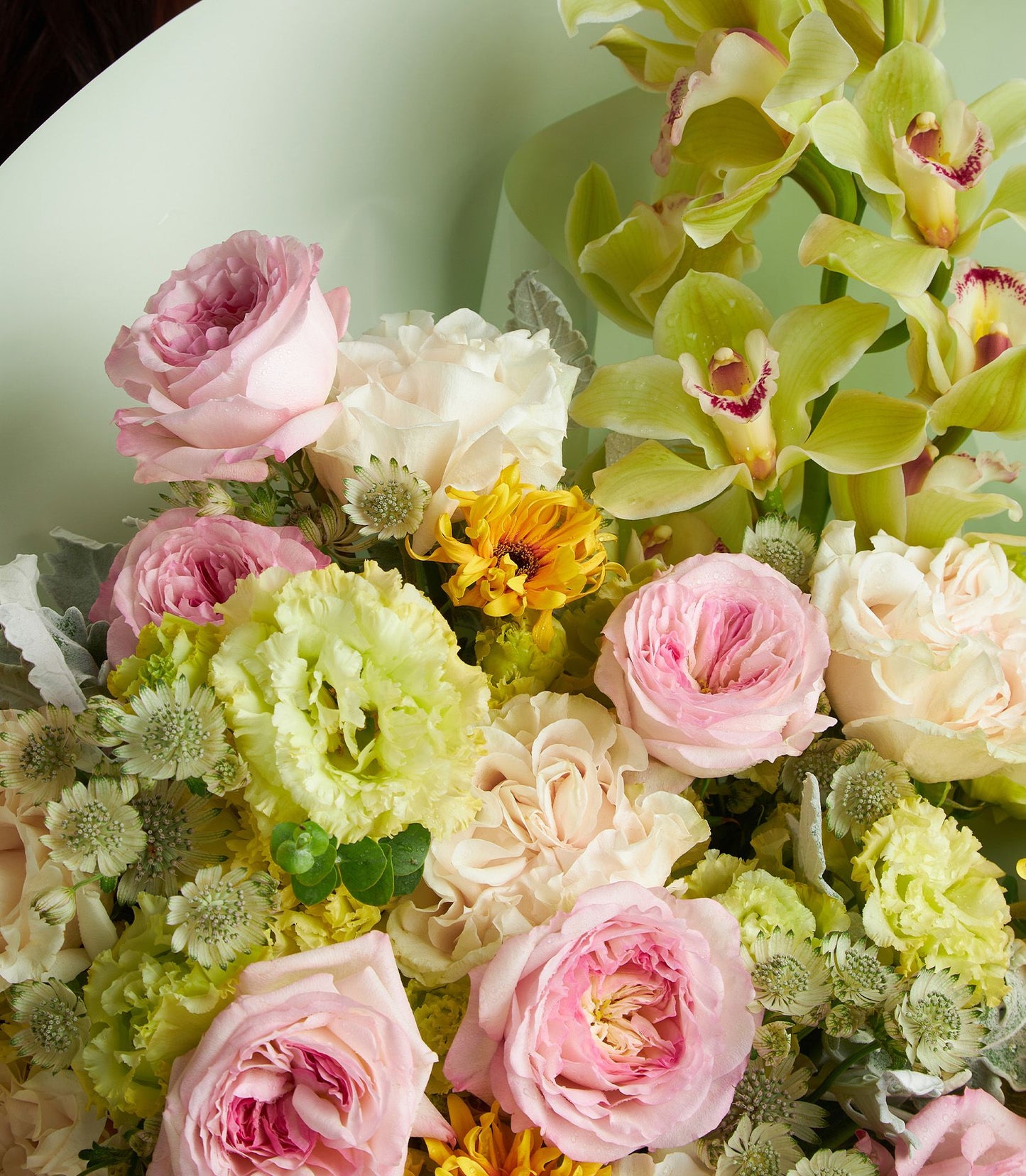 Pastel mixed flower bouquet with pink roses, white lisianthus, yellow mums, and chartreuse orchids in light green wrap