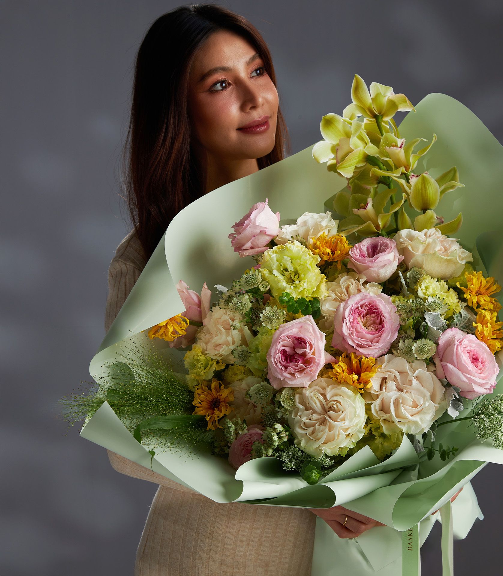 Pastel mixed flower bouquet with pink roses, cream roses, yellow chrysanthemums, and green orchids in sage paper wrap