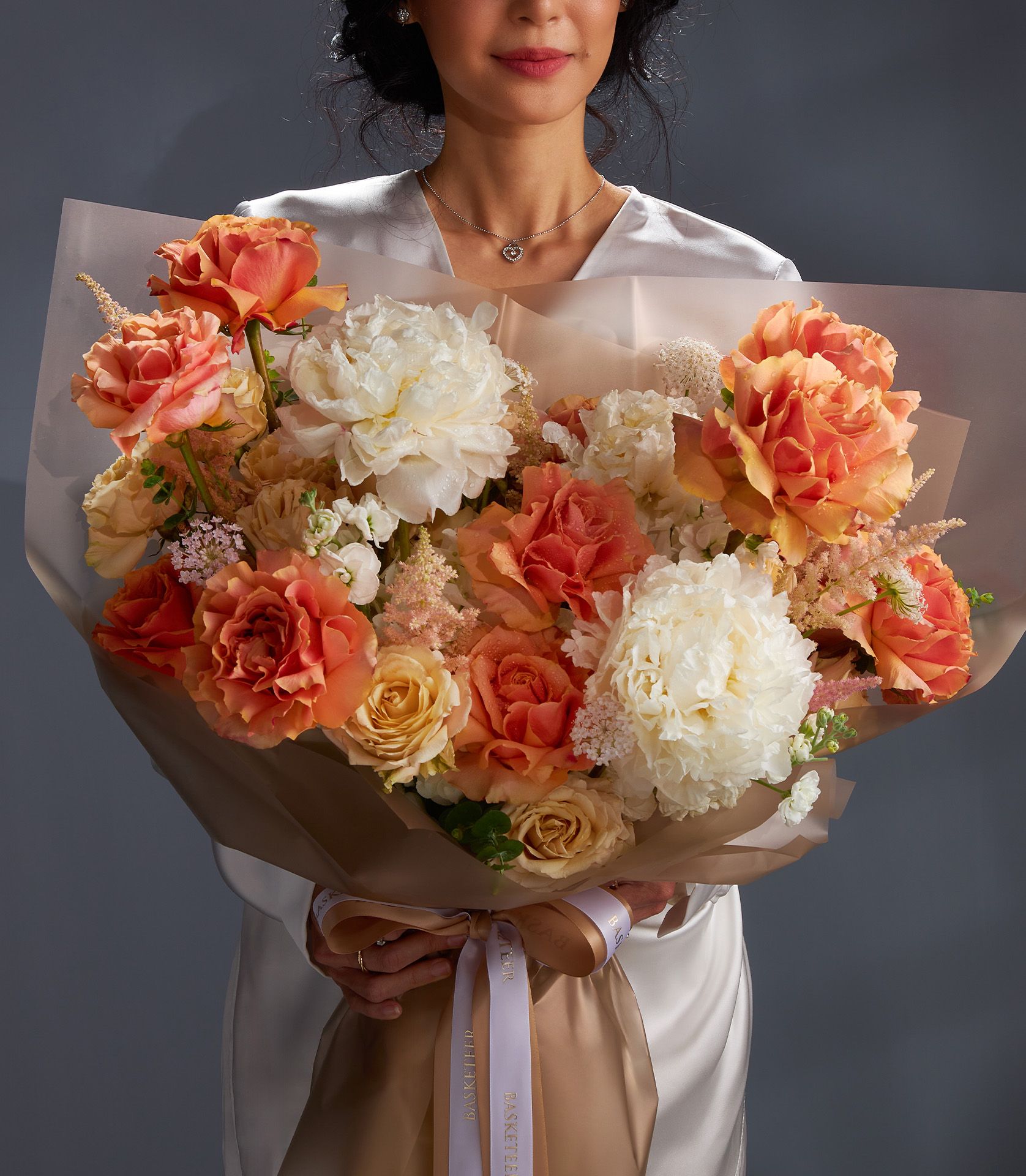 Luxury peony and rose bouquet in cream, peach, and orange with gold satin ribbon bow
