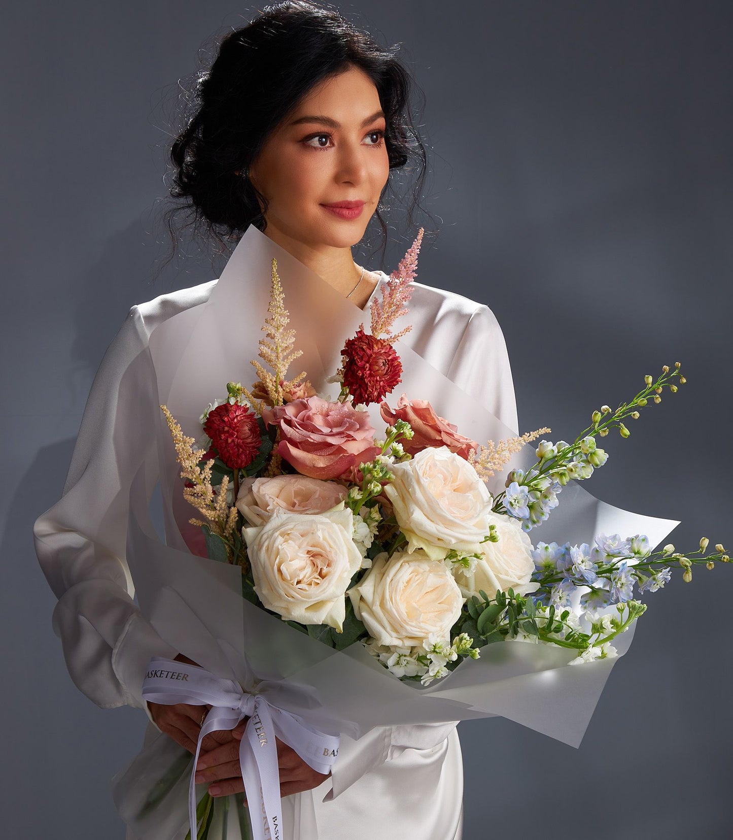 Elegant rose harmony bouquet with pink, cream, and red roses, delphiniums, and astilbe in white wrapping
