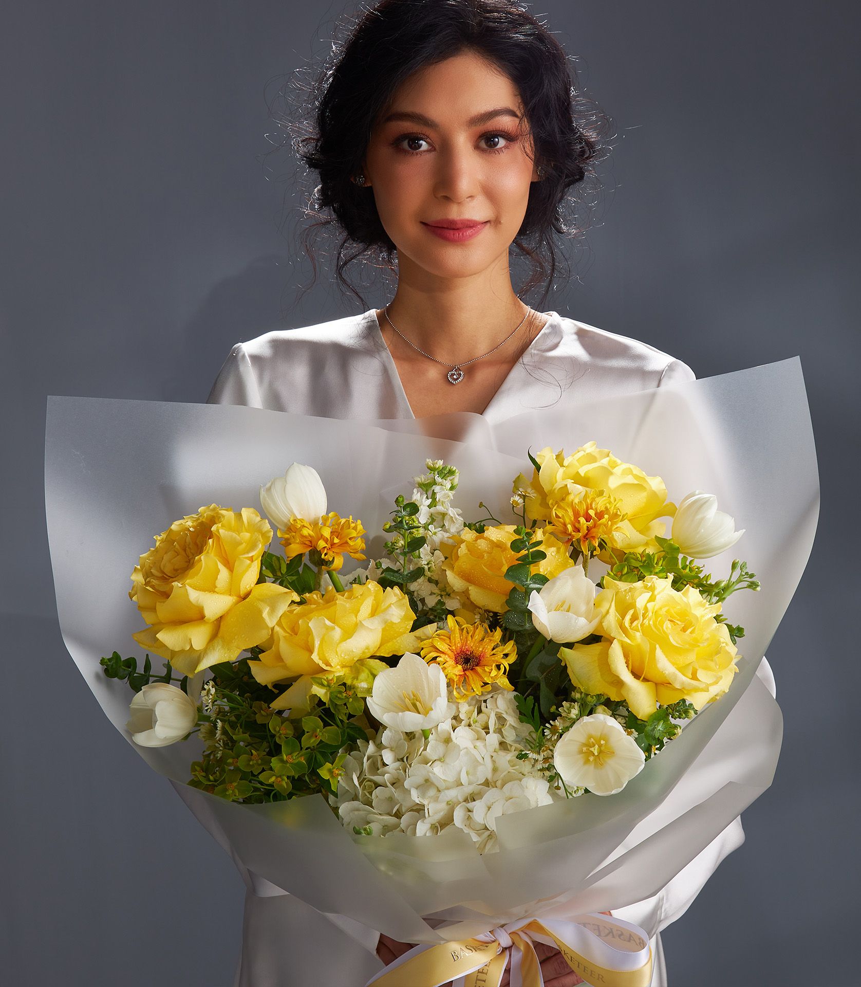 Sunshine yellow roses and white tulips fresh flower bouquet with hydrangeas and greenery, wrapped in white paper with gold