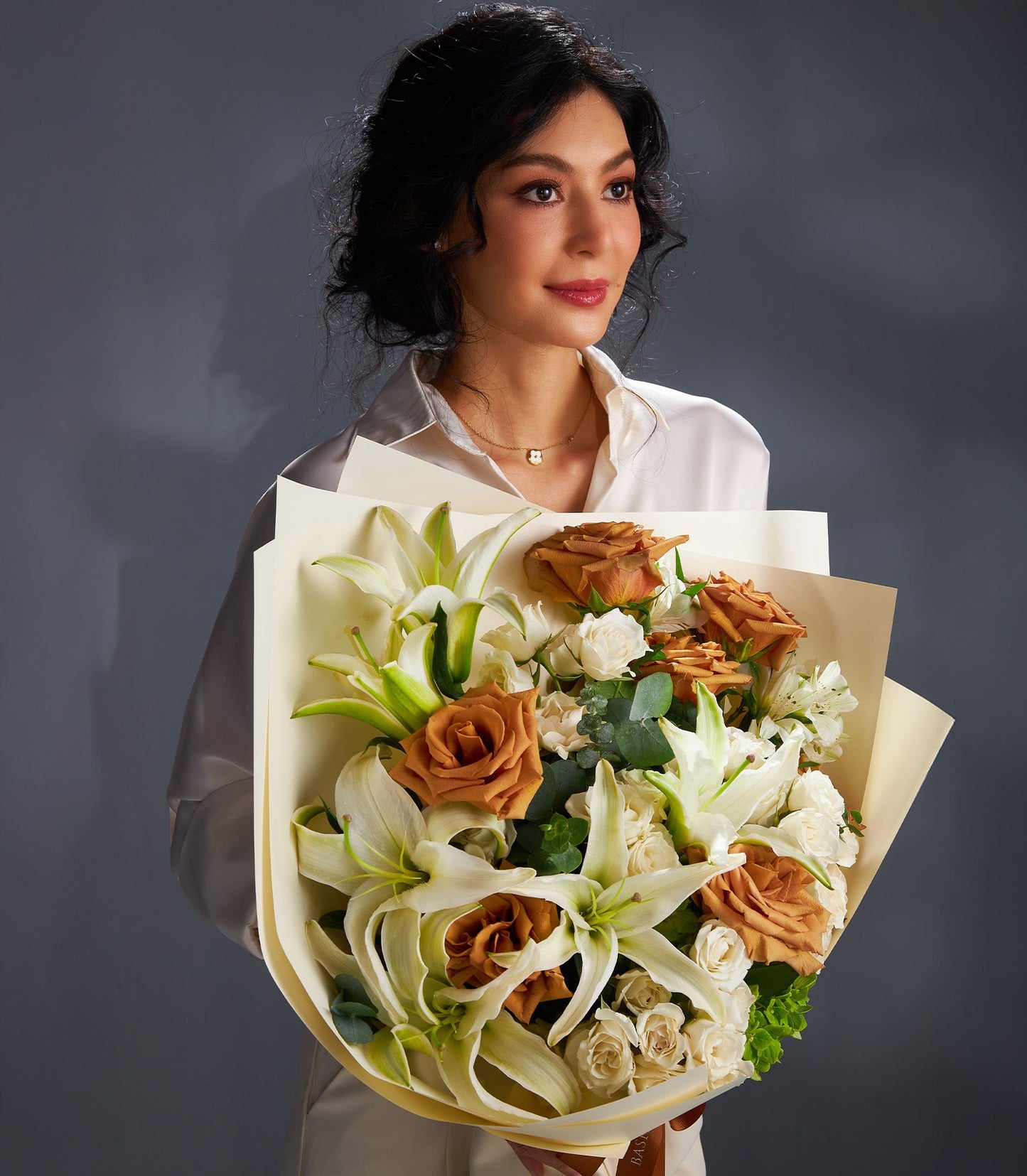 Woman holding luxury bouquet of white lilies and rust-orange roses with cream wrapping and brown ribbon