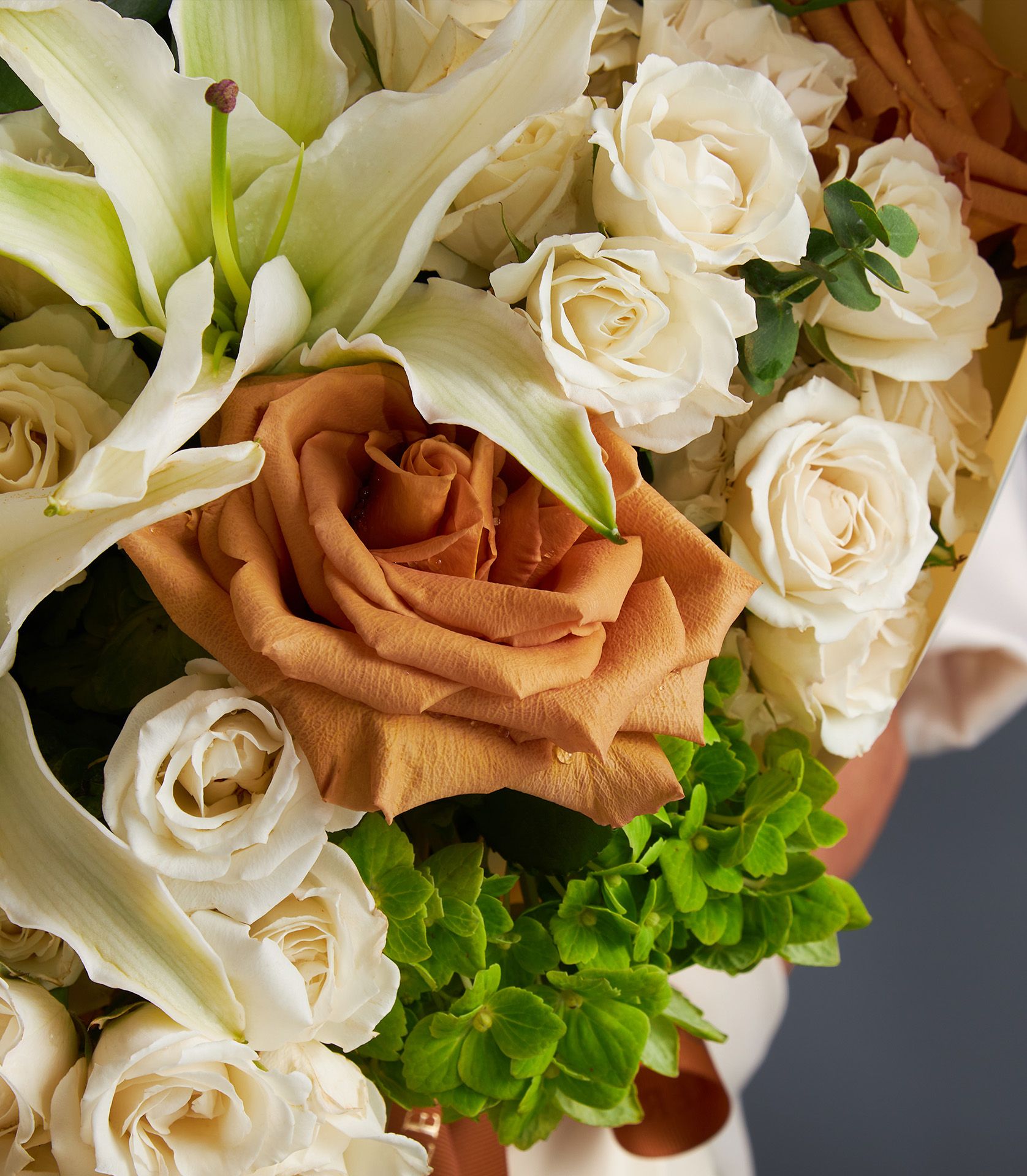 Luxury lily and rose bouquet with caramel rose, cream roses, and green hydrangea foliage wrapped in cream paper with brown