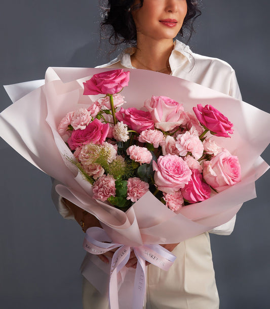 Blush pink rose and carnation bouquet with white accents, wrapped in soft pink paper and tied with ribbon