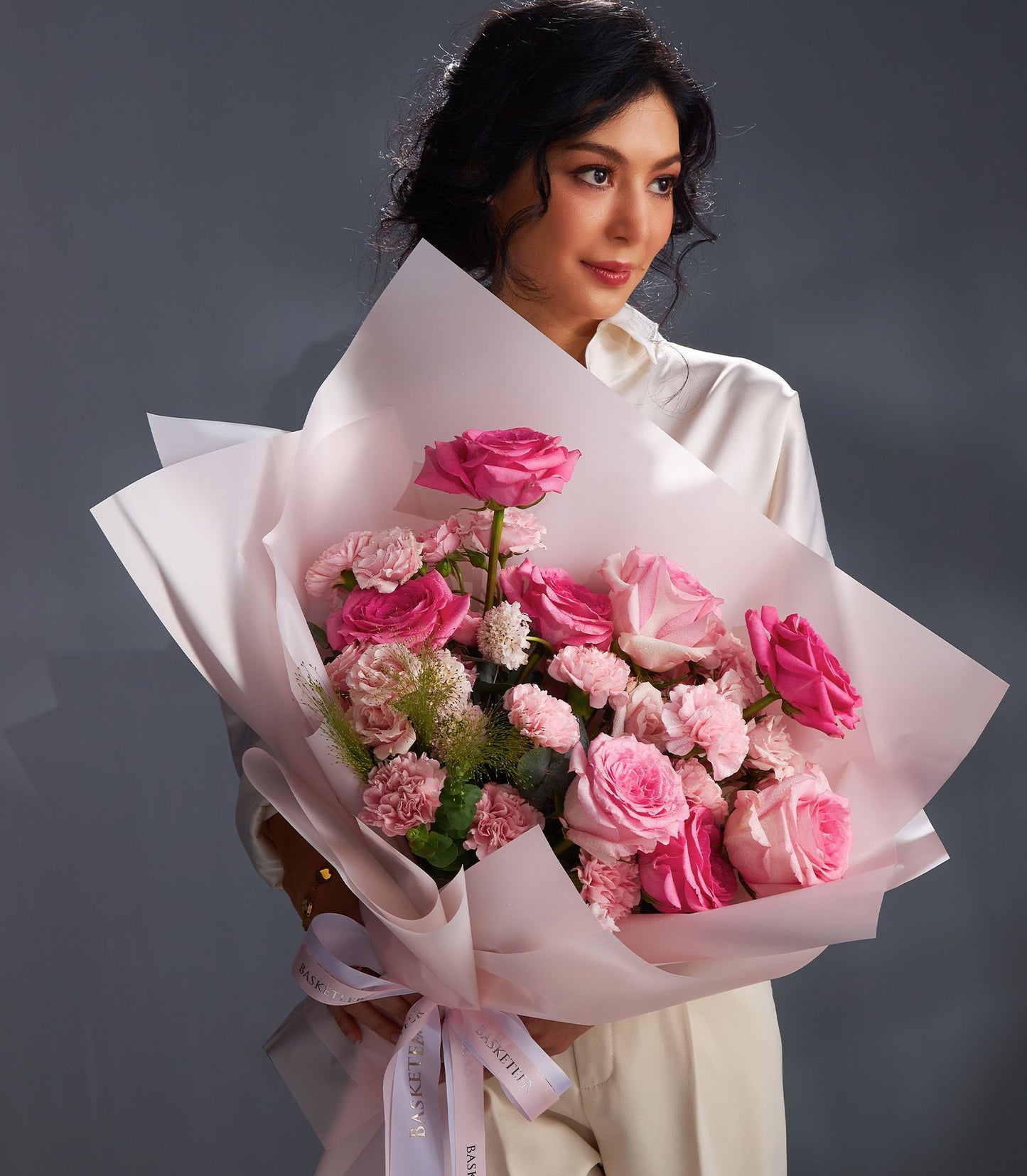 Woman holding premium pink rose and carnation bouquet with white ribbon, blush spring flowers for gifting