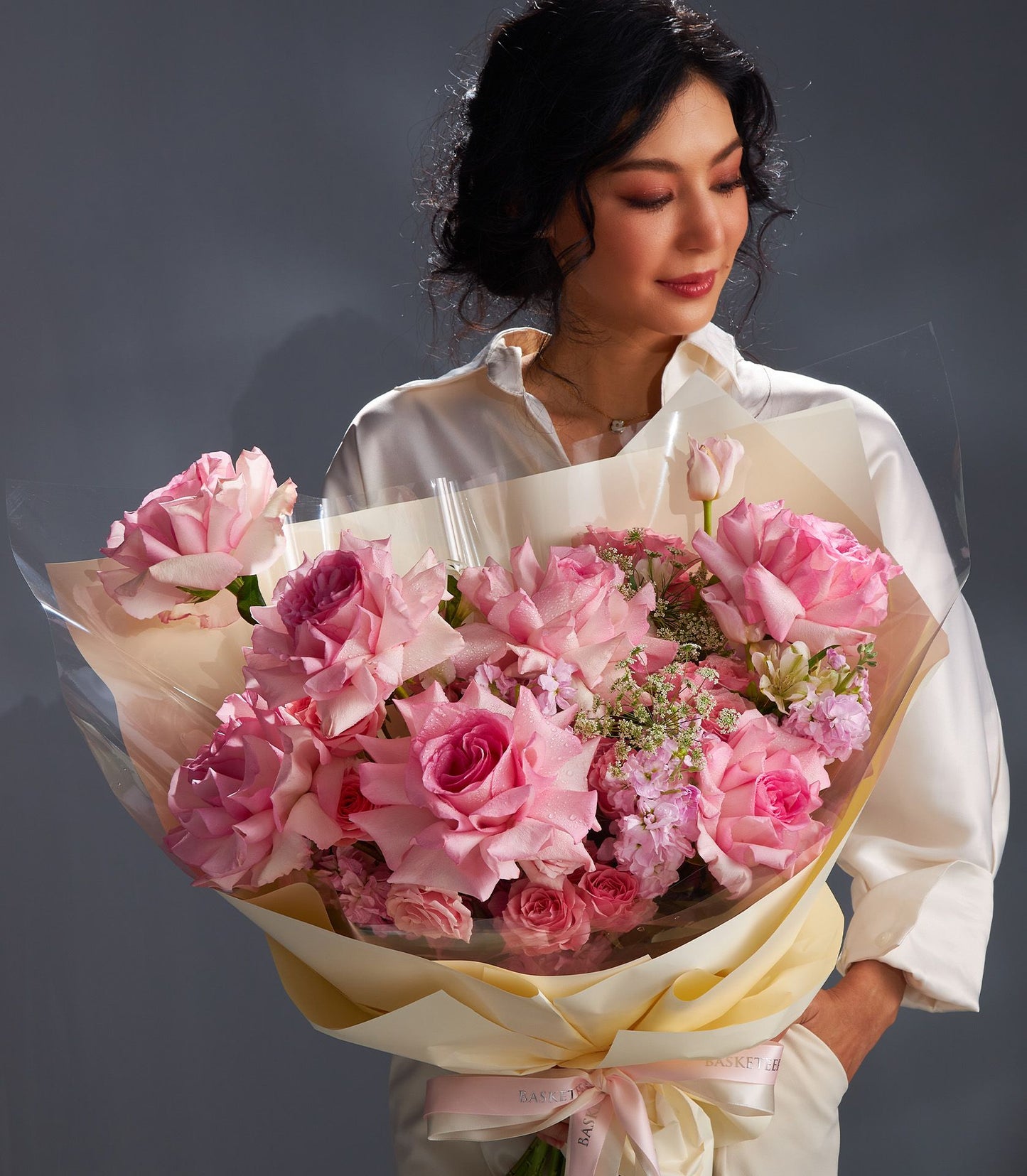 Pink rose bouquet with filler flowers in yellow paper wrap, held by woman in white shirt
