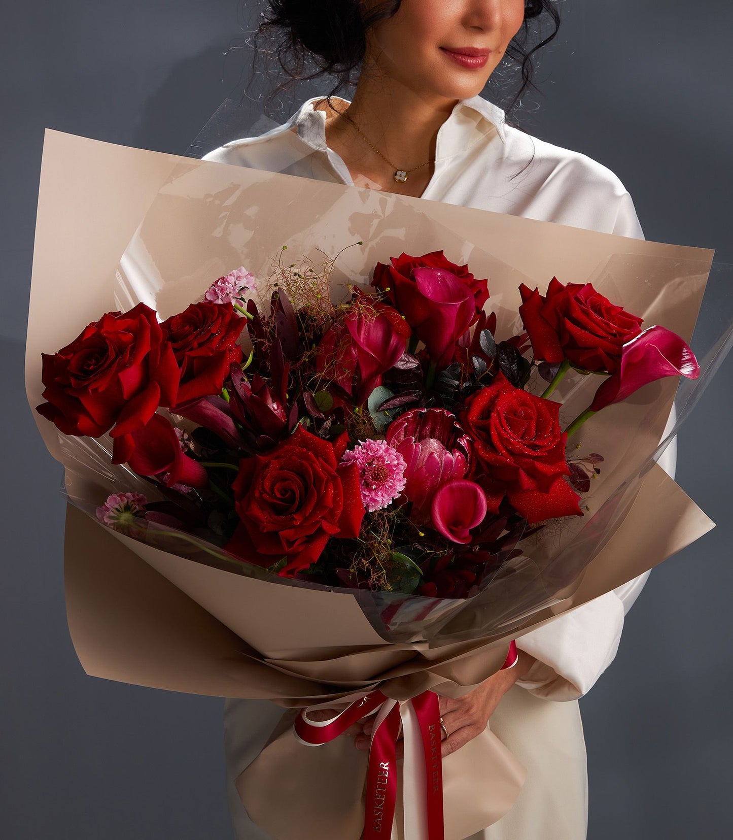 Vibrant red rose and pink calla lily bouquet with beige wrap and red ribbon