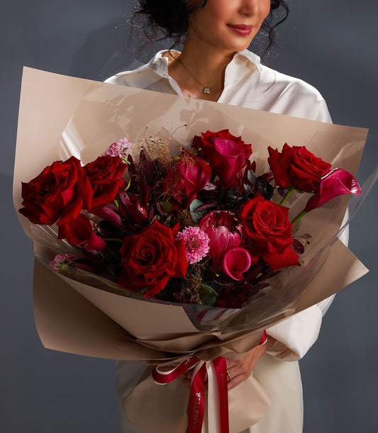 Vibrant red rose and pink calla lily bouquet with beige wrap and red ribbon