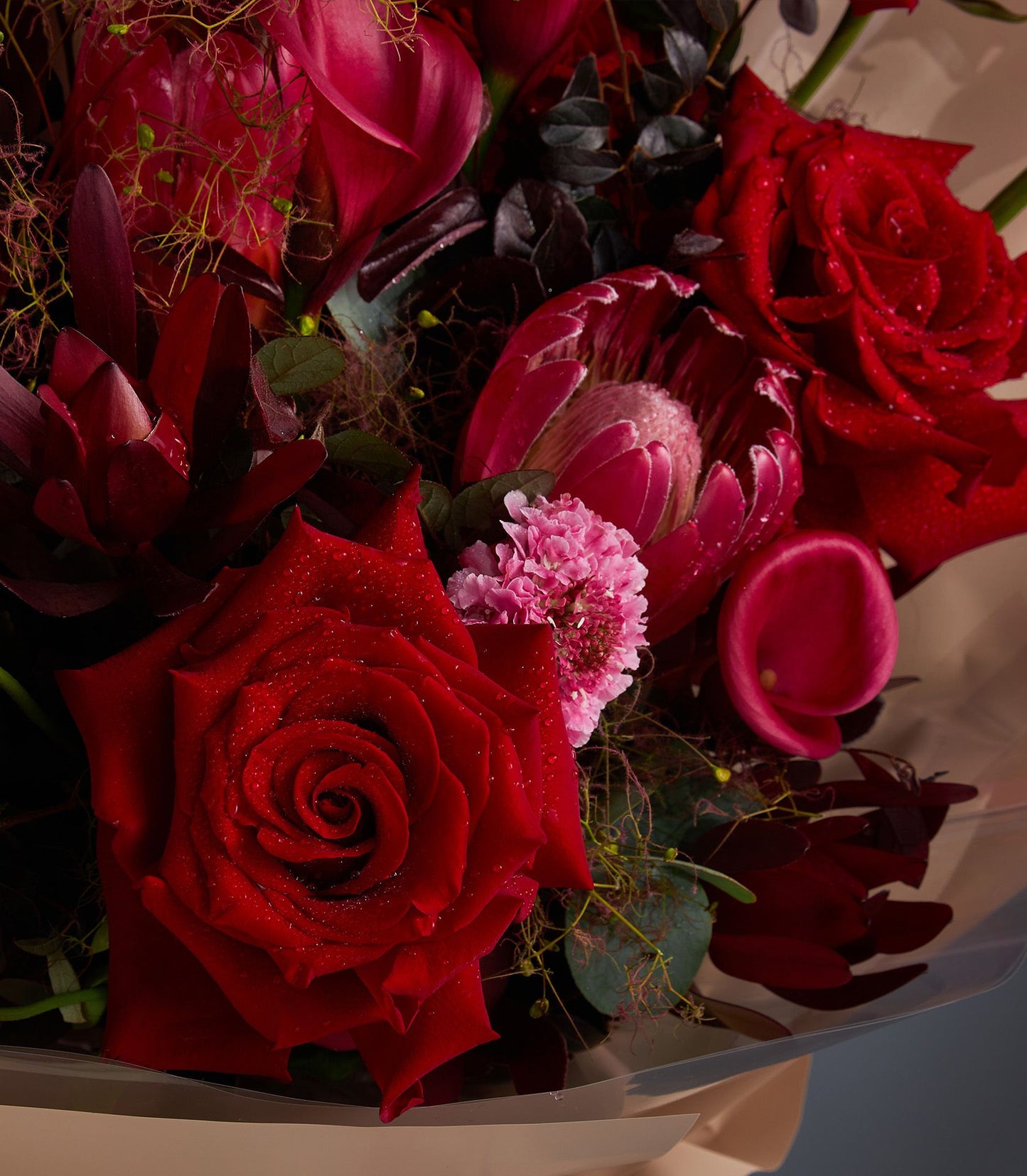 Vibrant crimson and fuchsia rose bouquet with fresh-cut roses and protea, artisan arrangement with lush green foliage