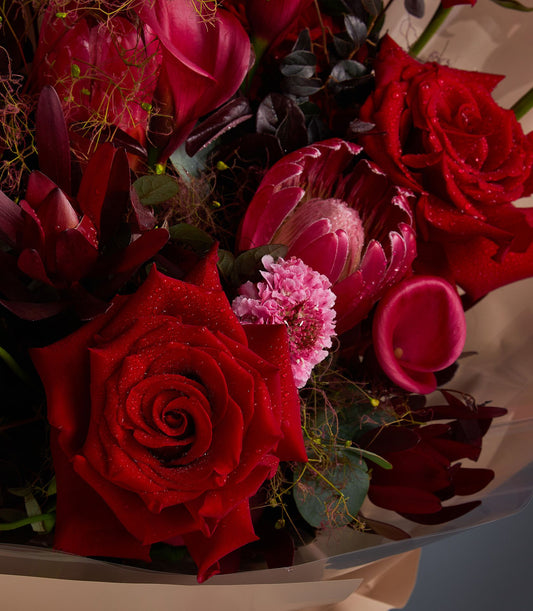 Vibrant crimson and fuchsia rose bouquet with fresh-cut roses and protea, artisan arrangement with lush green foliage