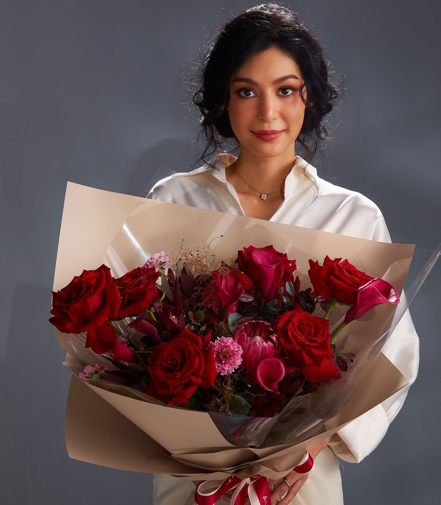 Woman holding large red rose and pink calla lily bouquet with greenery, wrapped in kraft paper and red ribbon