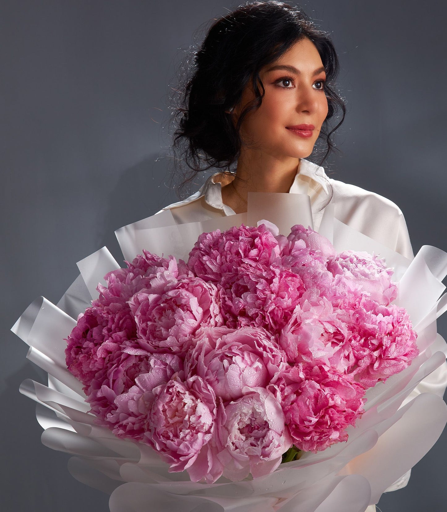 Woman holding large blush pink peony bouquet with fresh water droplets, wrapped in white paper