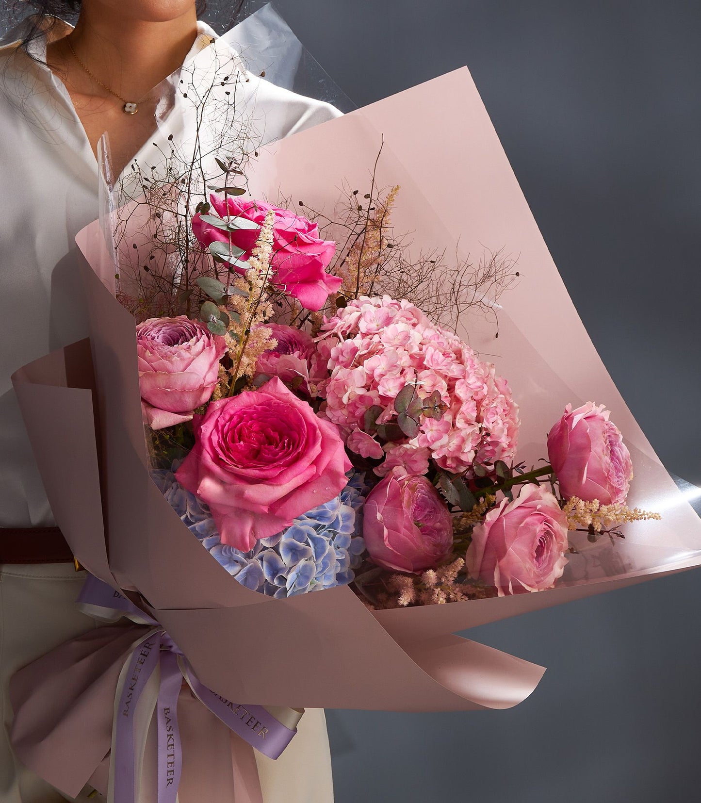Pink rose and hydrangea bouquet with eucalyptus, wrapped in light pink paper and purple ribbon