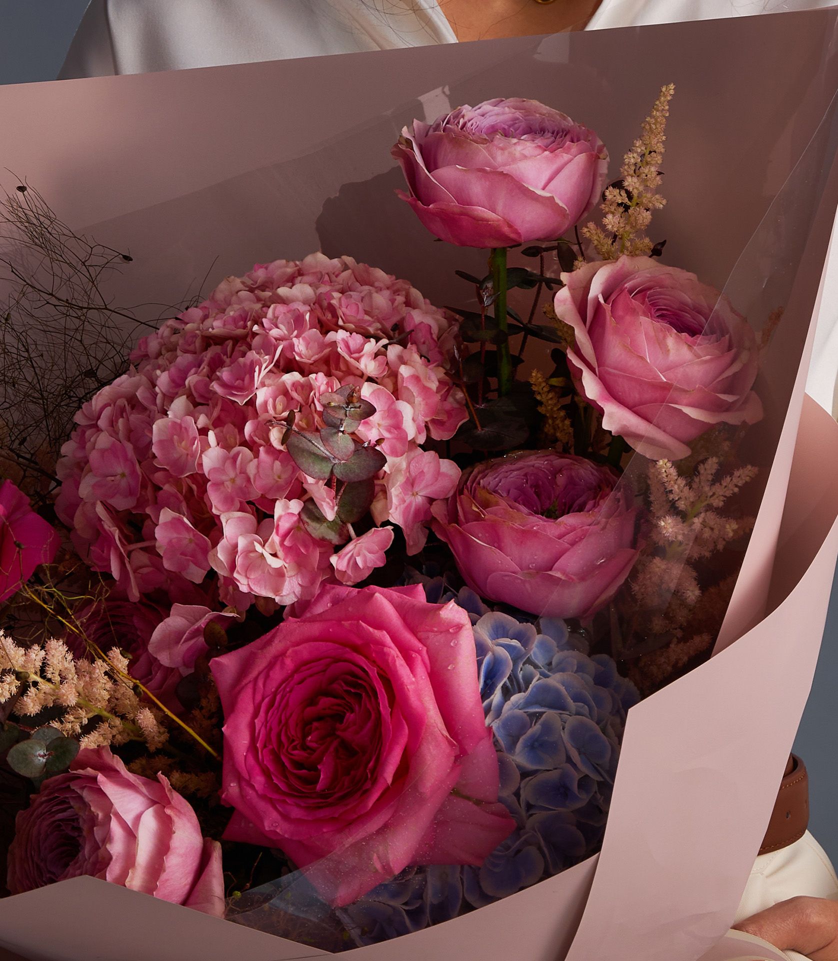 Fresh pink rose and hydrangea bouquet with textured dried branches, wrapped in soft pink paper