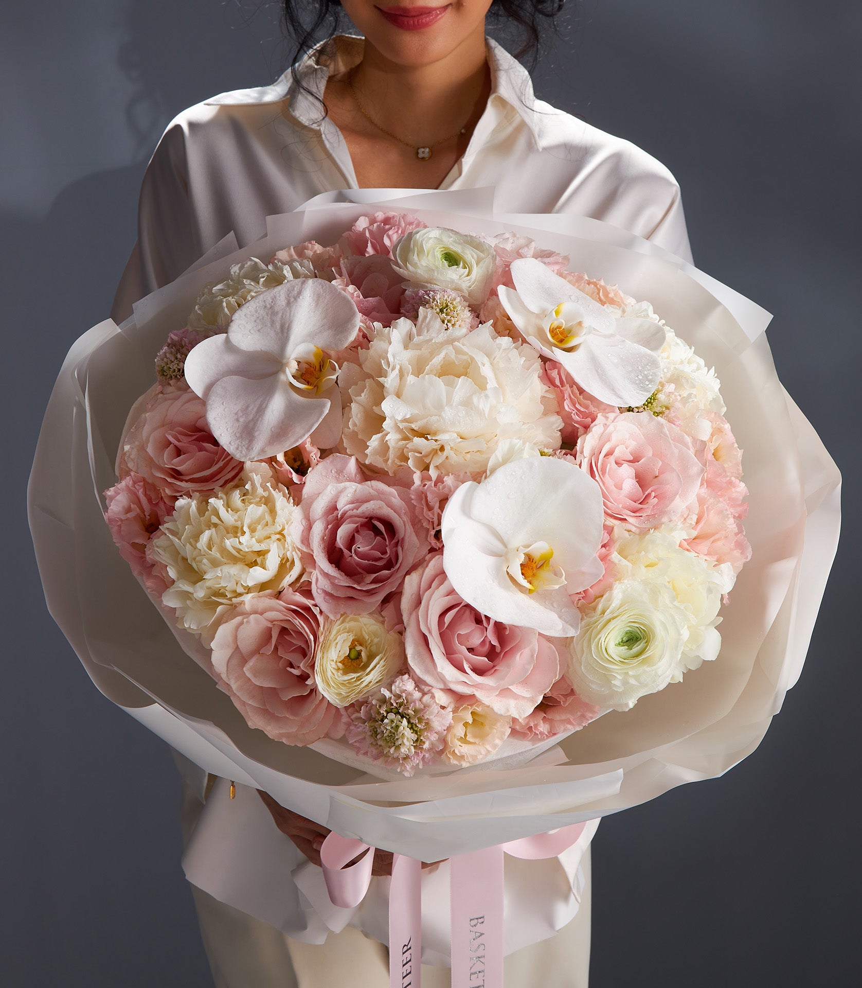 Premium mixed peony bouquet with roses, orchids, and ranunculus in soft pink and cream, wrapped in luxury tissue with silk