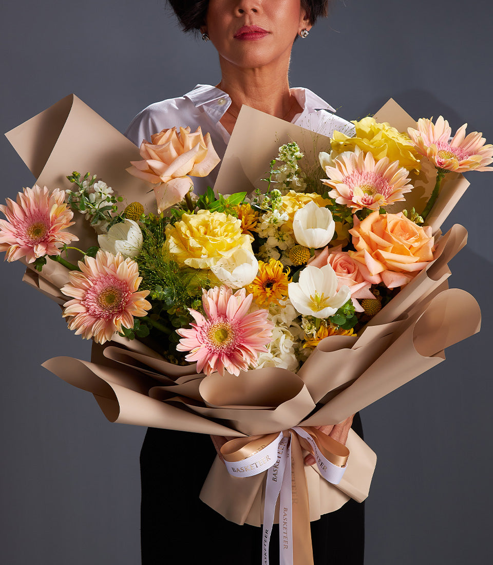 Vibrant mixed flower bouquet with pink gerberas, yellow roses, and white tulips in brown paper wrap